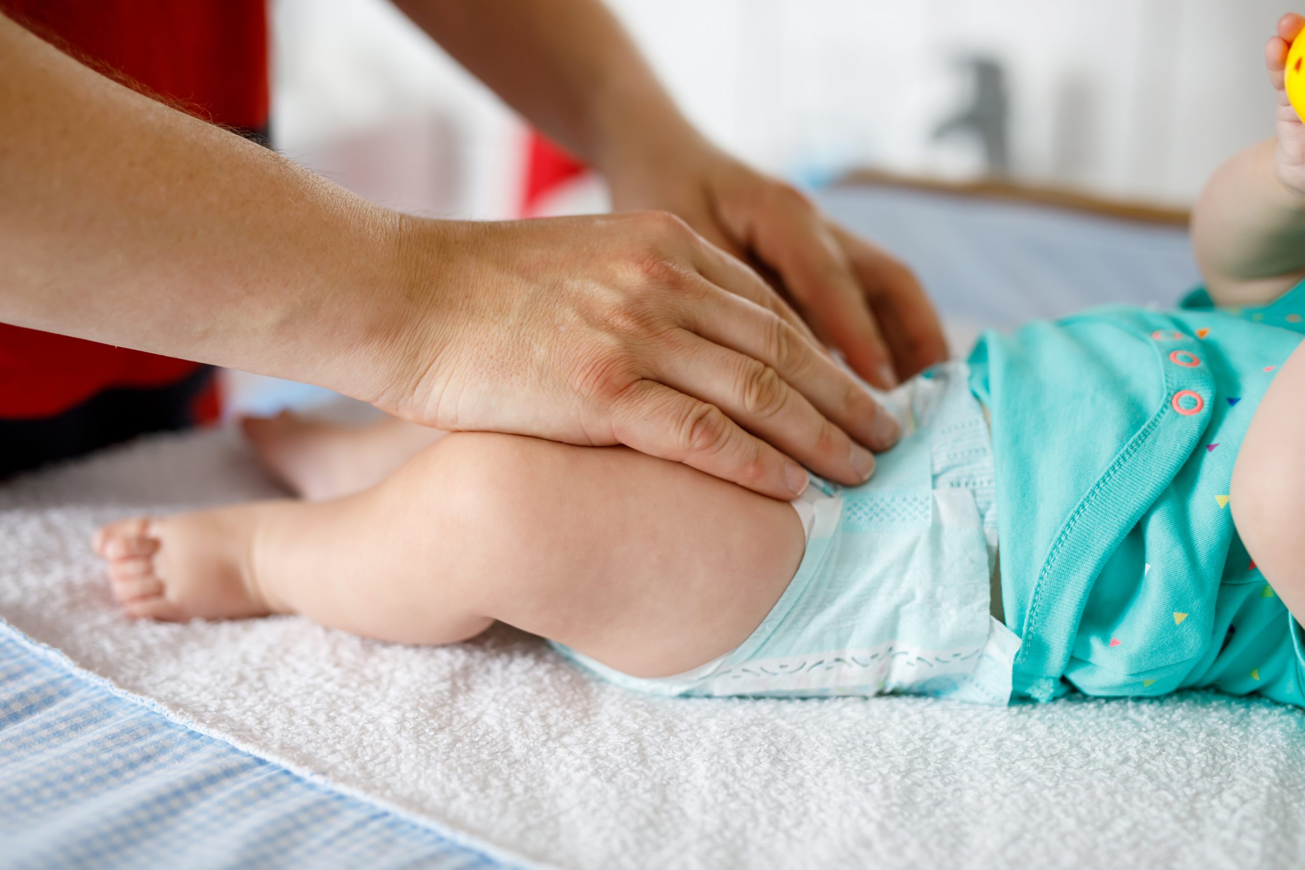 Close-up of father changing diaper of his newborn baby daughter. Little child, girl on changing table in bathroom with rattle toys